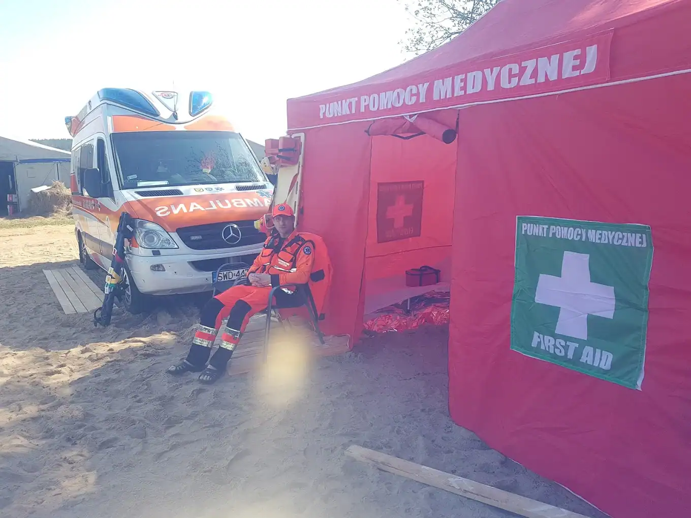 Ambulans medyczny i pielęgniarka w stroju ratunkowym przed punktem pomocy medycznej na plaży.
