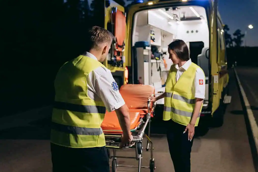 Emergency responders prepare a gurney for patient transport outside an ambulance under streetlights.